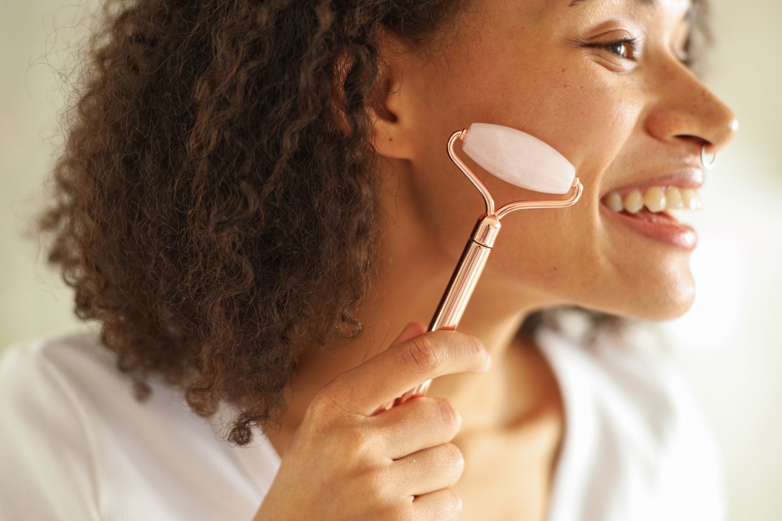 Woman smiling with facial roller on face, enhancing skin and facial features